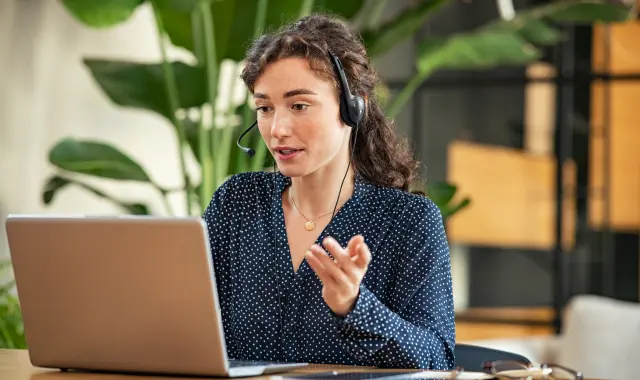 Woman with headphones at desk with laptop, focused on work.